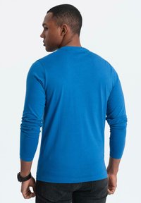 Langarm-T-Shirt in leuchtendem Blau, aus Baumwolle. Mit Rundhalsausschnitt und engen Ärmeln, kombiniert mit dunklen Hosen.