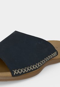 Μαύρο σανδάλι τύπου slip-on με ταμπά σόλα και διακοσμητικές λευκές σταυροβελονιές κατά μήκος της άκρης του πάνω λουριού.