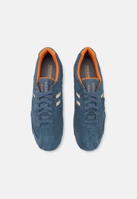 Baskets en daim bleu et en mesh avec des accents orange, dotées d'un système de laçage et de trois bandes blanches sur le côté. Texture respirante.