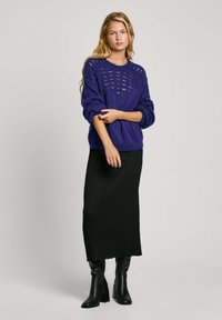 Lila stickad tröja med öppet mönster, kombinerad med en svart randig kjol. Svarta klackstövlar fulländar outfiten.