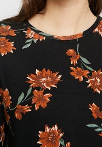 Primer plano de una camiseta negra con un escote redondo que presenta un patrón de flores naranjas y hojas verdes.