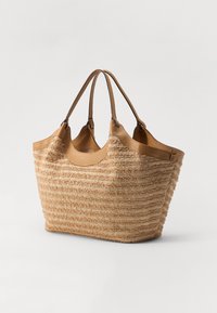 Sac en paille tissée couleur beige clair avec des rayures texturées. Il possède deux poignées en cuir robustes et un intérieur spacieux.