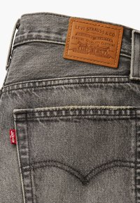 Gray denim jeans with a brown leather label at the waistband. Features red stitching and a distinct back pocket design with curved seams.