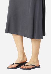 Wygodne klapki z teksturowaną granatową podeszwą i ciemnymi paskami, noszone z luźną ciemnoszarym sukienką. Stopy ustawione obok siebie.