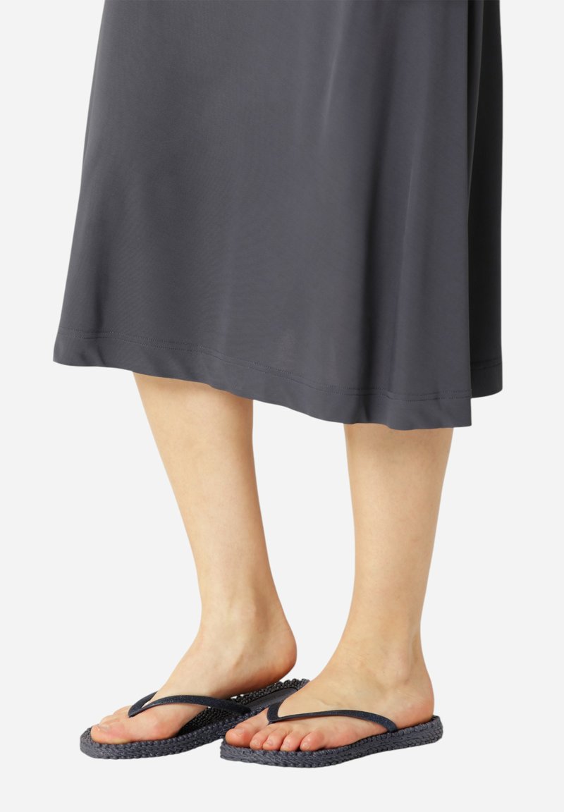 Wygodne klapki z teksturowaną granatową podeszwą i ciemnymi paskami, noszone z luźną ciemnoszarym sukienką. Stopy ustawione obok siebie.