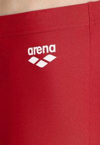 Rode zwembroek met een zachte textuur, voorzien van een wit "arena" logo en drie diamantvormen. De stof lijkt rekbaar en aansluitend te zijn.