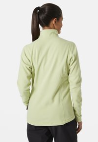 Jasnozielona polarowa kurtka z wysokim kołnierzem i dopasowanym krojem, z płaskimi szwami i miękką fakturą. Na dole widoczne czarne spodnie.