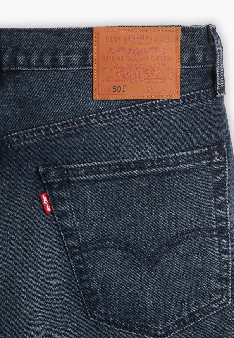 Ciemnoniebieskie dżinsy z skórzaną naszywką z napisem "Levi Strauss & Co." i "Lot 501." Posiadają czerwoną metkę Levi's oraz charakterystyczne przeszycie kieszeni tylnej.