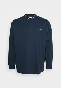 Marineblauwe polo met lange mouwen, gemaakt van katoen, met een mandarijnkraag, twee knopen en contrasterende witte accenten op de kraag en mouwen.