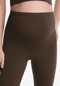 Bruna högmidjade leggings tillverkade av stretchigt tyg, med en slät yta och sömlös design som sträcker sig över magen.