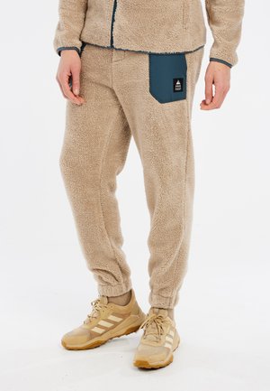 Beige fleece pants with a tapered leg, featuring a dark blue side pocket. The fabric has a textured, fluffy appearance.