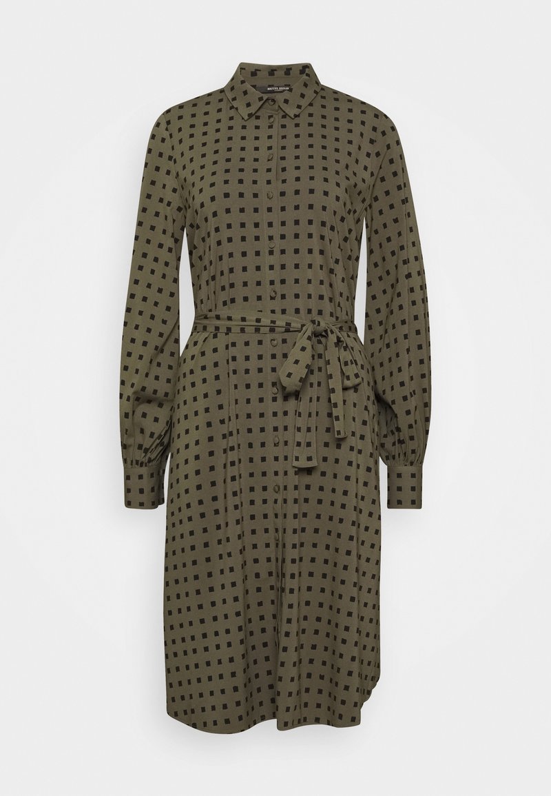 Robe-chemise vert olive longueur genou avec motif carré noir, manches longues, boutonnée devant, col et ceinture nouée à la taille.