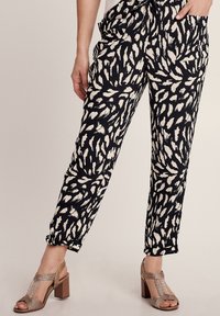 Zwarte broek met een wit abstract patroon, met een relaxte pasvorm, zakken en elastische boorden. Gecombineerd met metalen hoge sandalen.