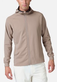 Beige letvægts zip-up hættetrøje med hætte, lange ærmer og en glat tekstur. Sømdetaljer løber langs skuldrene og ærmerne.
