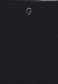 Tissu noir côtelé avec une texture lisse, orné d'un petit logo argenté en forme de "G". Le fond est d'un noir uni.