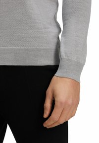 Maglione grigio a maglia con scollo rotondo, polsini e orlo a costine. La traspirabilità è morbida e leggera, abbinata a pantaloni neri aderenti.