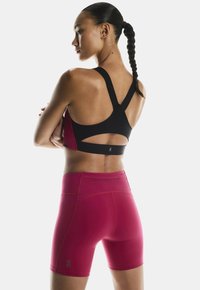 Black and red athletic sports bra with a racerback design, paired with fitted pink shorts featuring a logo and seam detailing.