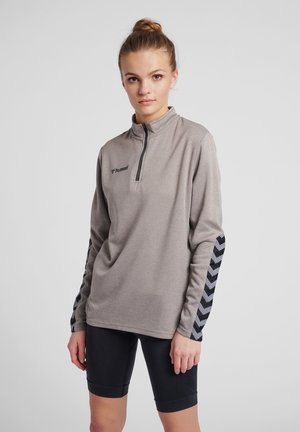 Light gray quarter-zip pullover with black chevron pattern on sleeves, made of textured fabric, paired with black cycling shorts.