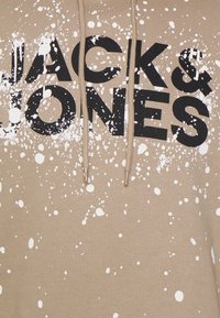 Felpa beige con testo nero "JACK & JONES" e design con macchie di vernice bianche, dotata di lacci beige.