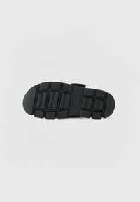 Black rubber shoe sole with a textured surface, featuring deep tread patterns and a rectangular indent for added grip and flexibility.