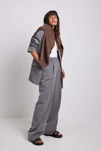 Costume gris ajusté avec pantalon à jambes larges, t-shirt blanc et châle en maille marron. Pour compléter le look, des sandales noires à enfiler avec des brides texturées.