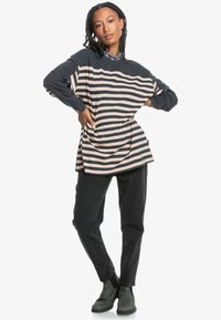 Long-sleeve striped sweatshirt in navy and light pink, relaxed fit, with a round neckline and ribbed cuffs, paired with black jeans and ankle boots.