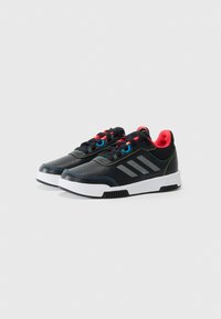 Baskets noires de sport avec une finition texturée, présentant une semelle blanche, des accents rouges et bleus, et trois bandes grises sur le côté.