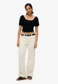 Sort kortærmet cropped top med puffærmer, parret med højtaljede, brede beige bukser og et sort bælte. Sandaler fuldender outfittet.