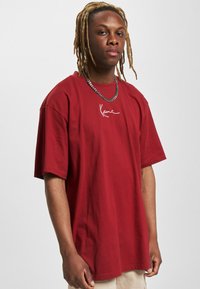Bordeaux oversized t-shirt i bomuld med korte ærmer, der har et hvidt skriftlogo på brystet og en afslappet pasform.