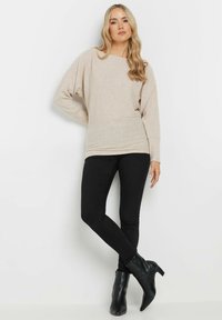 Beige neulepaita, jossa on leveä kaula-aukko ja ribbikuvio, yhdistetty mustiin skinny-farkkuihin ja mustiin nilkkureihin.