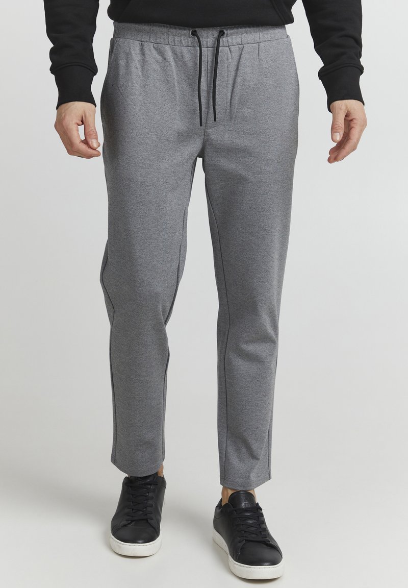 Grå joggerbukser med snor i taljen, tætsiddende pasform, sidelommer og kontrasterende sort piping, parret med sorte sneakers.