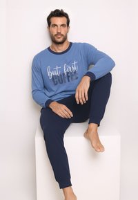Blue cotton long-sleeve shirt with "but first coffee" graphic, paired with navy pants; smooth texture and fitted design.