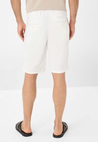 White shorts with a casual fit, featuring back pockets and button details, paired with black sandals. The fabric appears lightweight and smooth.