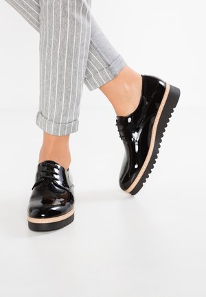 Zwarte lakleren veterschoenen met een dikke, gestructureerde zool en een accent in natuurlijke kleur langs de onderrand.