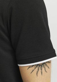 Zwarte polo met een gestructureerde stof, korte mouwen en een witte gestreepte accent langs de mouwzoom.