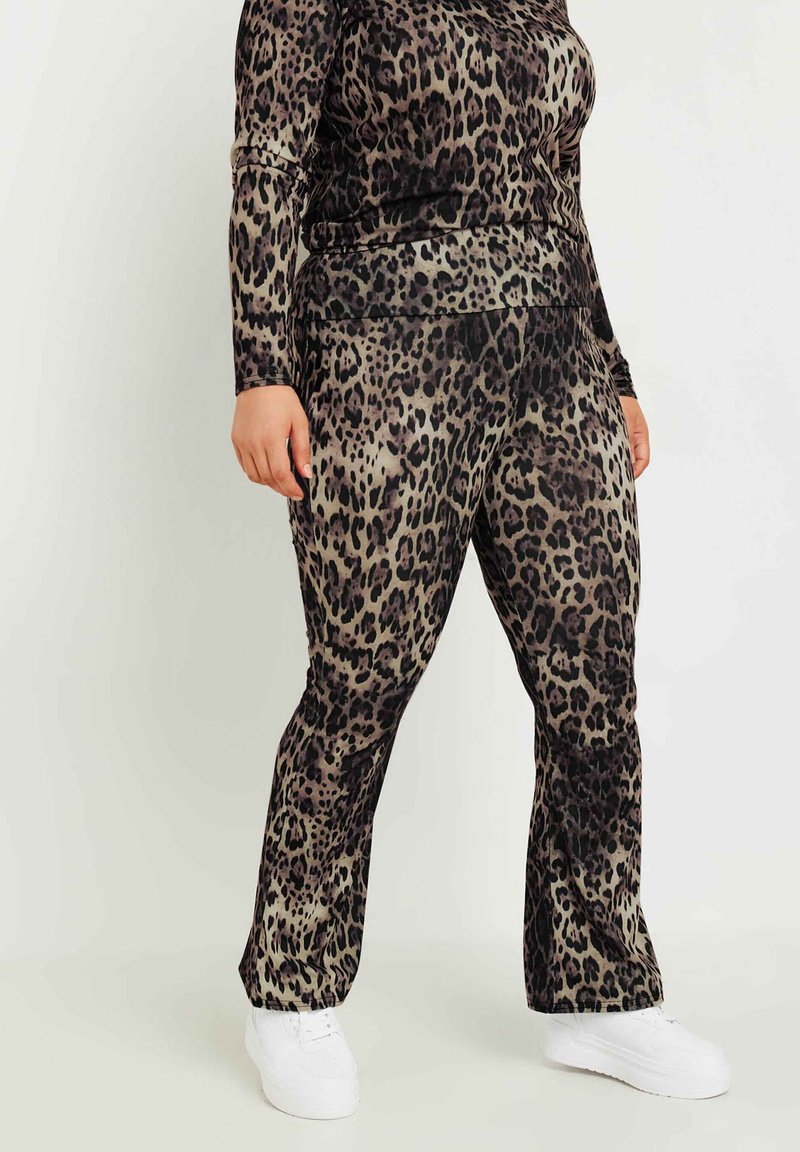 Leopardmönstrad, stretchig velouroutfit med långa ärmar och vida byxor. Färgerna inkluderar nyanser av brunt, svart och beige. Vita sneakers.