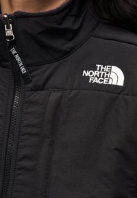 Μαύρο μπουφάν από απαλό, ελαφρύ υλικό. Διαθέτει ψηλό γιακά, φερμουάρ και κεντημένο λευκό λογότυπο "The North Face".