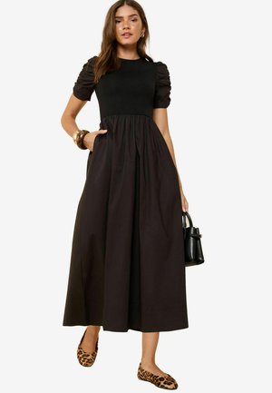 Schwarzes Kleid mit Puffärmeln, enganliegendem Oberteil und fließendem Rock. Das Model kombinierte es mit einer schwarzen Handtasche und Ballerinas im Leopardenmuster.