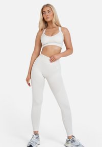 Witte sportbeha en high-waisted leggings van geweven stof. Beschikt over een naadloos ontwerp en een contrasterend logo op de linkerheup.