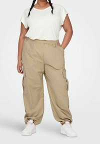 Pantaloni cargo beige con vita elastica e tasche laterali, abbinati a una maglietta bianca a maniche corte e scarpe da ginnastica bianche.