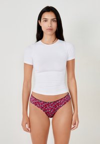Top bianco a maniche corte dal design aderente, abbinato a pantaloni bikini con motivo floreale caratterizzati da accenti rossi, blu e neri.