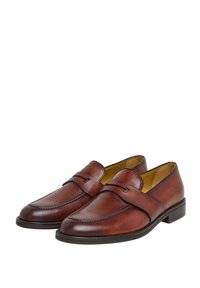 Bruna läderskor i loafermodell med en mjuk textur, rund tå och dekorativ rem över framfoten. Svart gummisula. Klassisk design.