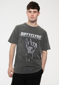 Gray cotton t-shirt with a relaxed fit, featuring white text and graphic design of a figure with bagpipes. Short sleeves and crew neck.