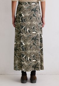 Jupe verte à fleurs présentant de grandes fleurs beige contourées, fabriquée en tissu léger, avec un design fluide, longueur cheville et fente latérale.