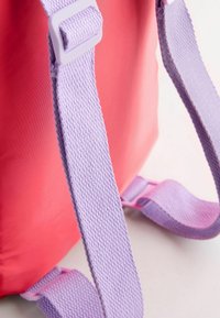 Ryggsäck med en rosa kropp, texturerade lavendelslingor och lila detaljer. Slingorna har ett vävt mönster och justerbara fästen.