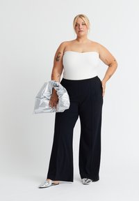 Haut sans manches texturé blanc à rayures, pantalon noir à jambes larges, sac argenté brillant et ballerines métalliques. Mettez l'accent sur des lignes épurées et des textures contrastées.