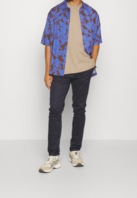 Koszula z krótkim rękawem w niebieski wzór na beżowej koszulce, zestawiona z ciemnymi spodniami i beżowymi trampkami. Ozdobiona motywami kwiatowymi i zwierzęcymi.