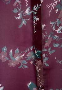 Flowy fabric in burgundy with floral patterns in teal, pink, and cream. Features a seamless design and smooth texture.