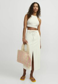 Top corto de lino de color claro y falda de talle alto con abertura; bolsa de mimbre en beige y rosa; chanclas amarillas.