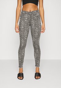Leggings de estampado de serpiente en blanco y negro con un diseño ajustado, que cuentan con una tela texturizada y una cinturilla elástica. Llevados con sandalias negras tipo slide.